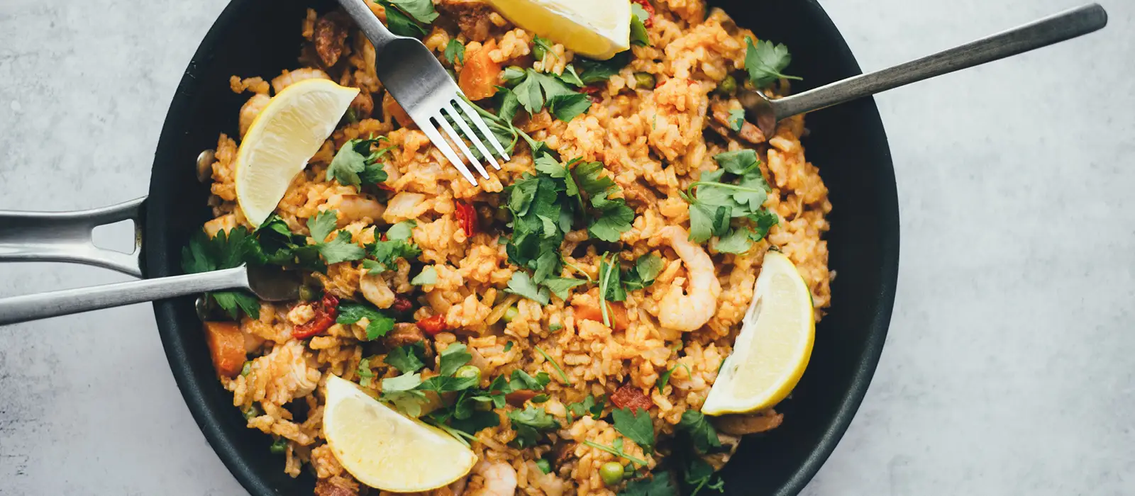 Bowl of paella with rice, prawns, lemon and herbs