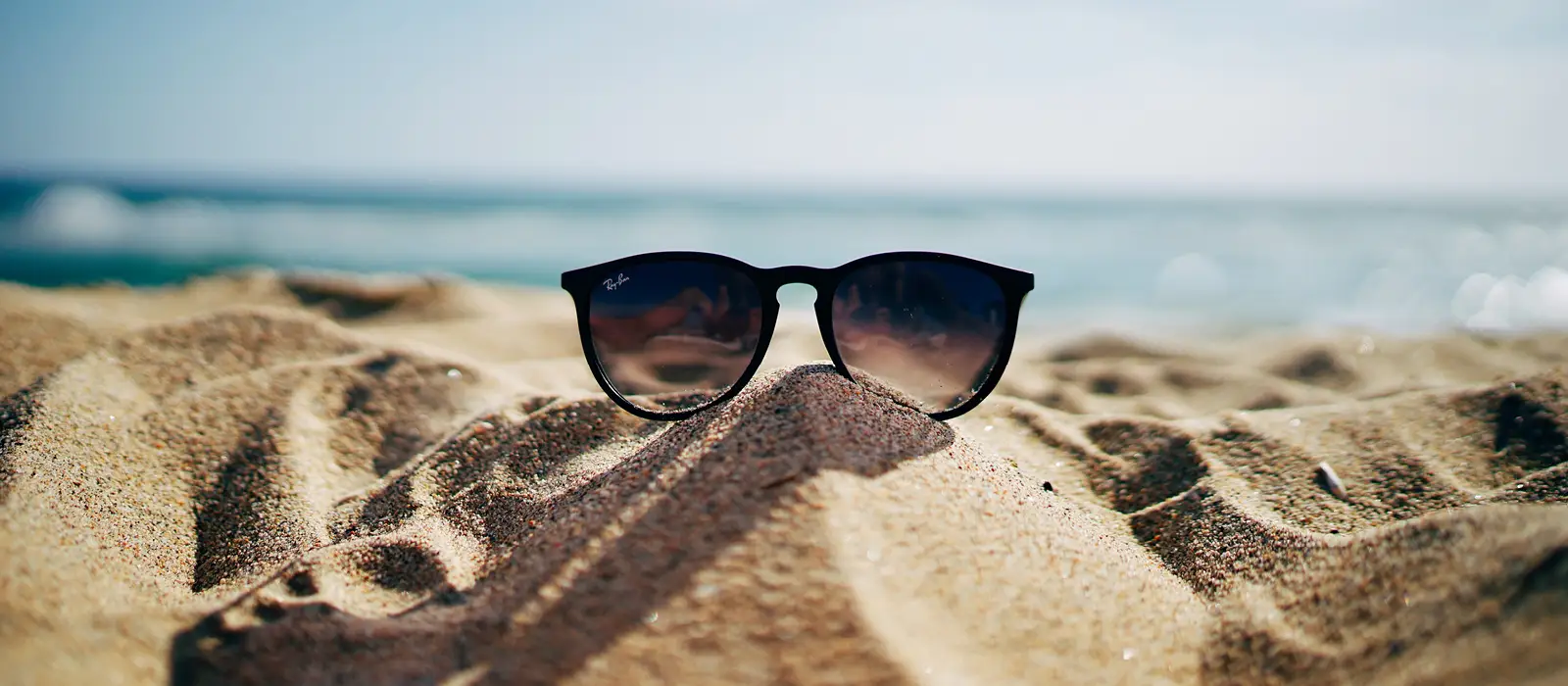 Pair of sunglasses sitting in sand at the beach