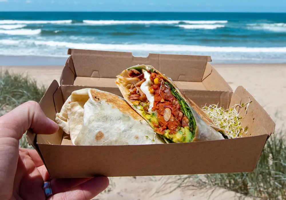 Breakfast Burrito in takeaway box with beach in the background