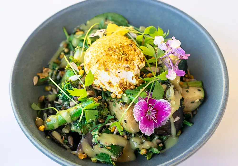 Bowl filled with green veggies, poached egg and dukkah